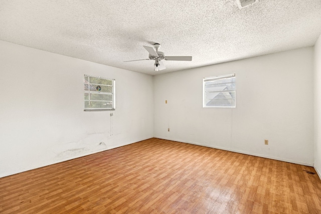 empty room with a wealth of natural light, wood finished floors, ceiling fan, and a textured ceiling