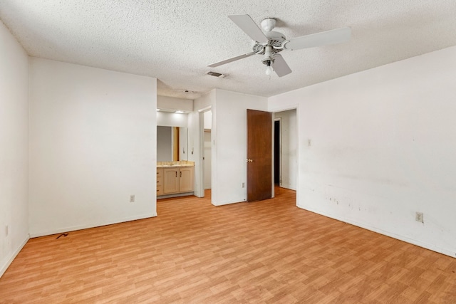 unfurnished bedroom featuring a textured ceiling, ensuite bathroom, baseboards, visible vents, and light wood-style floors