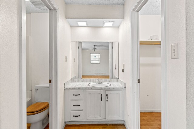 bathroom with a textured ceiling, vanity, ceiling fan, hardwood / wood-style flooring, and toilet