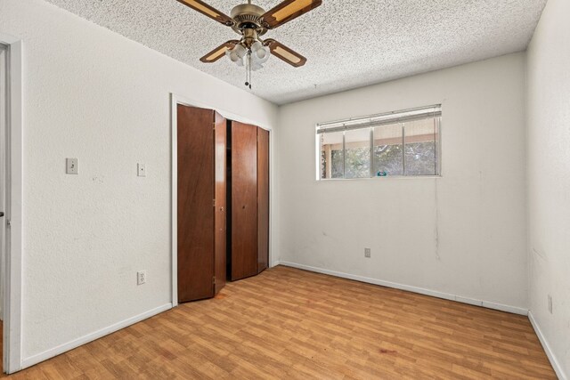 unfurnished bedroom with ceiling fan, light wood-type flooring, a textured ceiling, and a closet