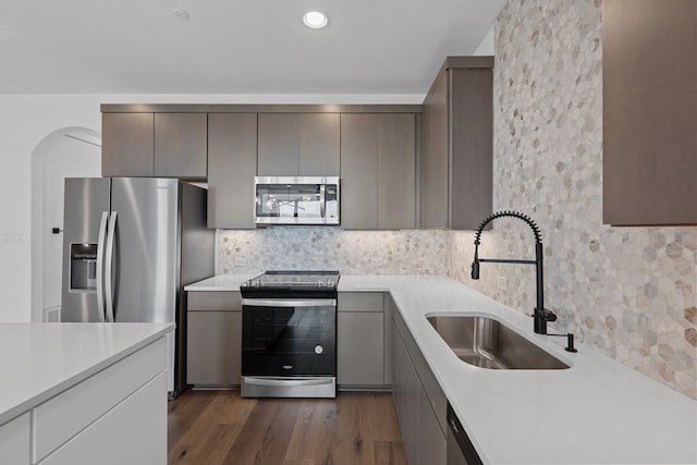 kitchen featuring sink, dark hardwood / wood-style floors, gray cabinets, appliances with stainless steel finishes, and tasteful backsplash