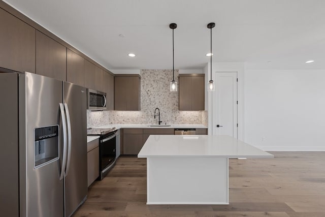 kitchen with appliances with stainless steel finishes, light wood-type flooring, sink, decorative light fixtures, and a kitchen island