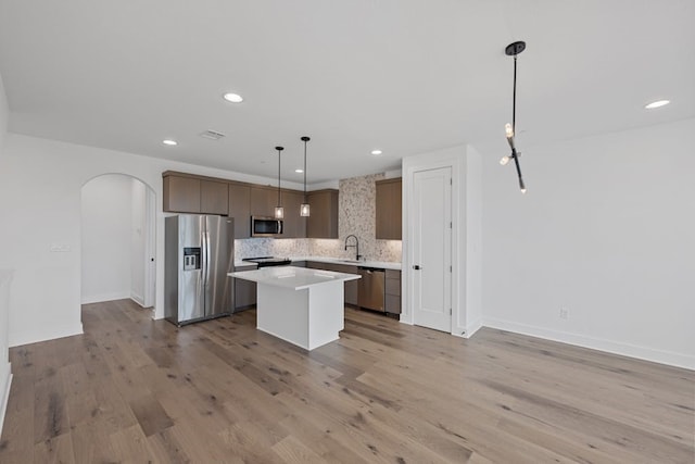 kitchen featuring appliances with stainless steel finishes, light wood-type flooring, a kitchen island, and pendant lighting