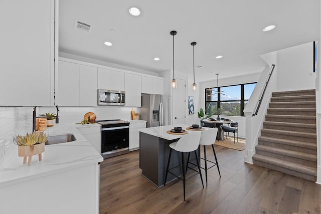 kitchen with appliances with stainless steel finishes, pendant lighting, white cabinets, dark hardwood / wood-style floors, and a kitchen island