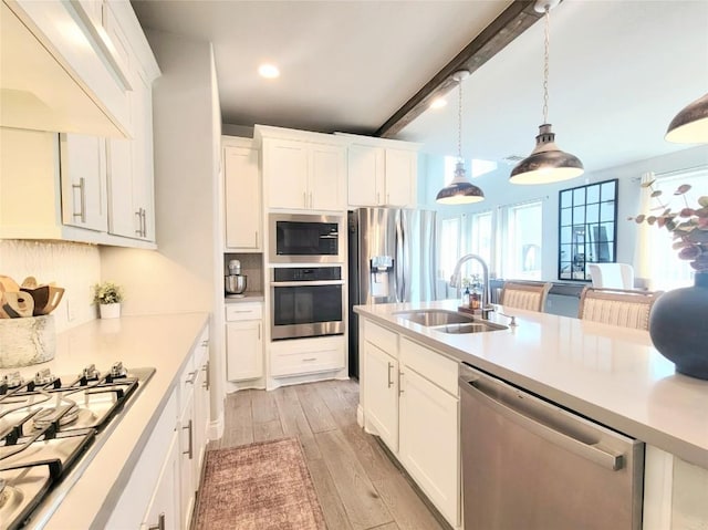 kitchen featuring beam ceiling, white cabinetry, sink, stainless steel appliances, and pendant lighting