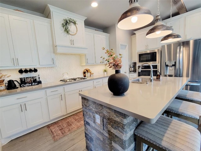 kitchen with pendant lighting, custom exhaust hood, white cabinets, sink, and appliances with stainless steel finishes