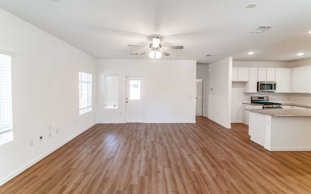 kitchen with light wood-type flooring, light stone countertops, ceiling fan, white cabinets, and appliances with stainless steel finishes