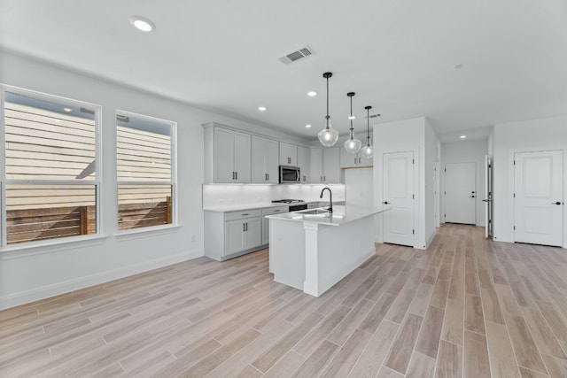 kitchen with a center island with sink, decorative light fixtures, light wood-type flooring, and sink