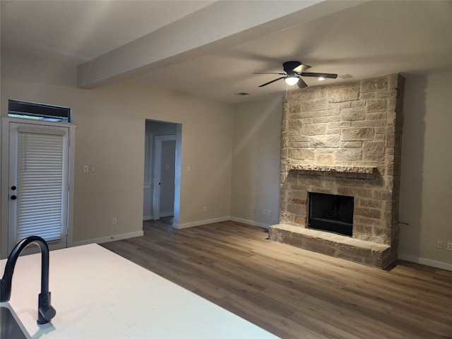 unfurnished living room with a stone fireplace, ceiling fan, and dark hardwood / wood-style flooring