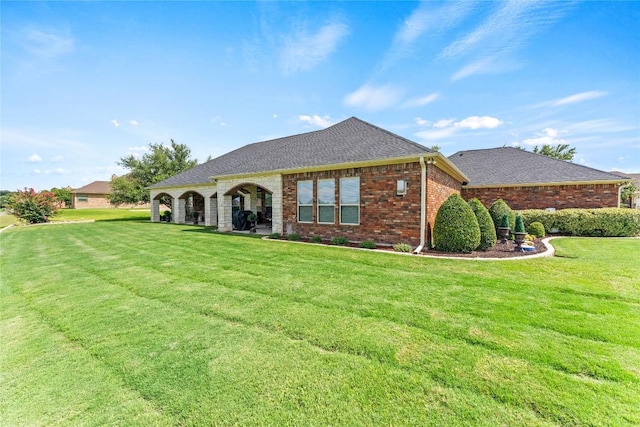 single story home with a shingled roof, a front lawn, and brick siding