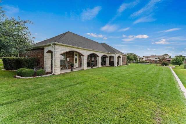 back of property featuring brick siding, a shingled roof, a patio, and a yard