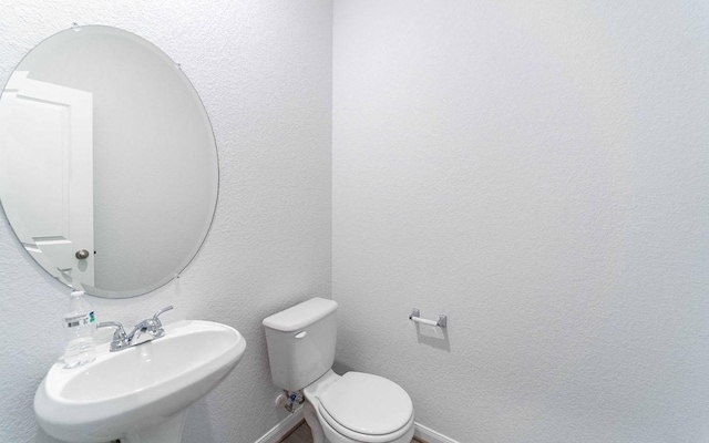 bathroom with a textured wall, a sink, and toilet