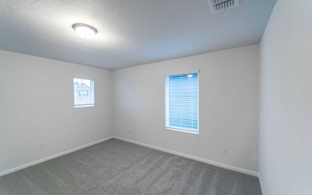 carpeted spare room featuring a textured ceiling, visible vents, and baseboards