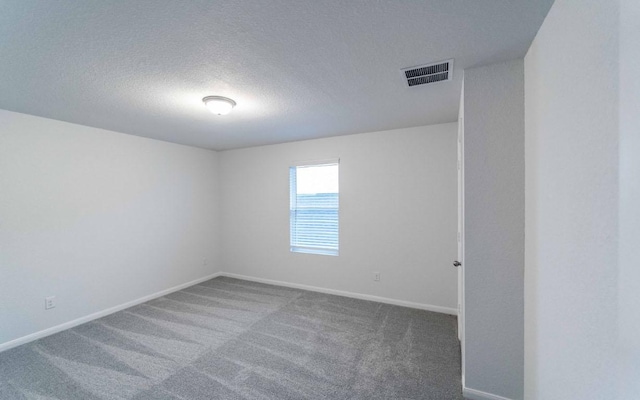 spare room featuring carpet, visible vents, a textured ceiling, and baseboards