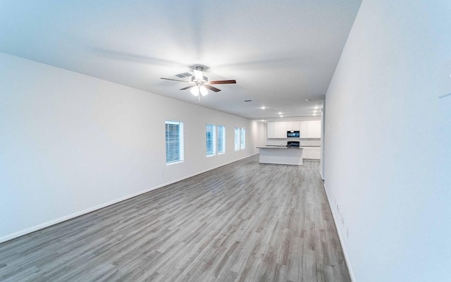 unfurnished living room featuring visible vents, light wood-type flooring, a ceiling fan, and baseboards