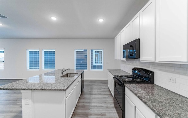 kitchen featuring a center island with sink, backsplash, a sink, wood finished floors, and black appliances