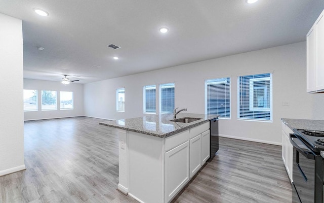 kitchen with light stone counters, light wood-style flooring, a sink, visible vents, and black appliances