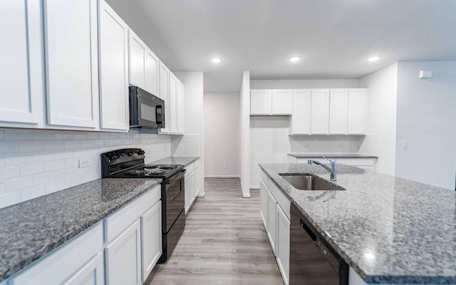 kitchen with light wood-style floors, white cabinets, a sink, dark stone counters, and black appliances