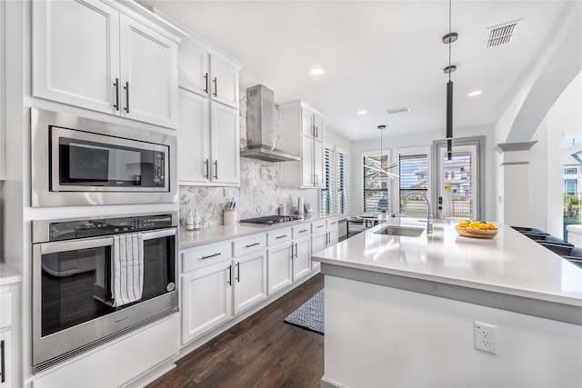 kitchen featuring appliances with stainless steel finishes, decorative light fixtures, wall chimney range hood, white cabinets, and sink