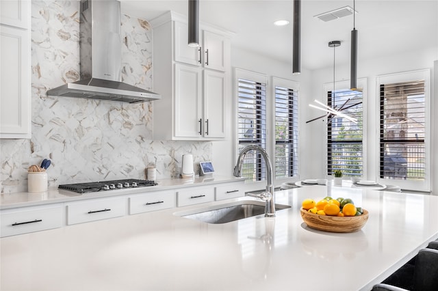 kitchen featuring wall chimney exhaust hood, decorative light fixtures, white cabinetry, decorative backsplash, and sink