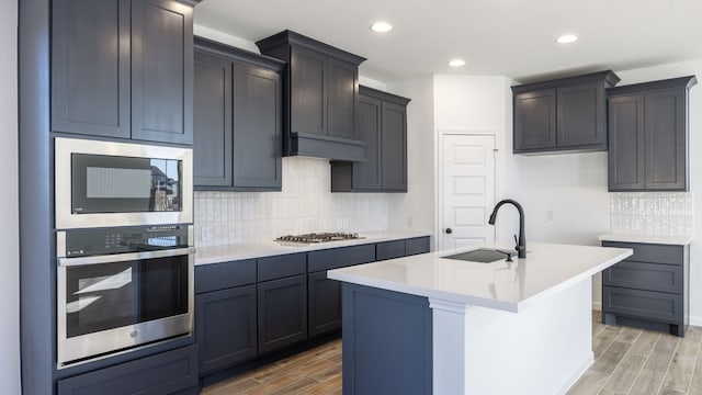 kitchen with hardwood / wood-style flooring, tasteful backsplash, sink, a kitchen island with sink, and appliances with stainless steel finishes