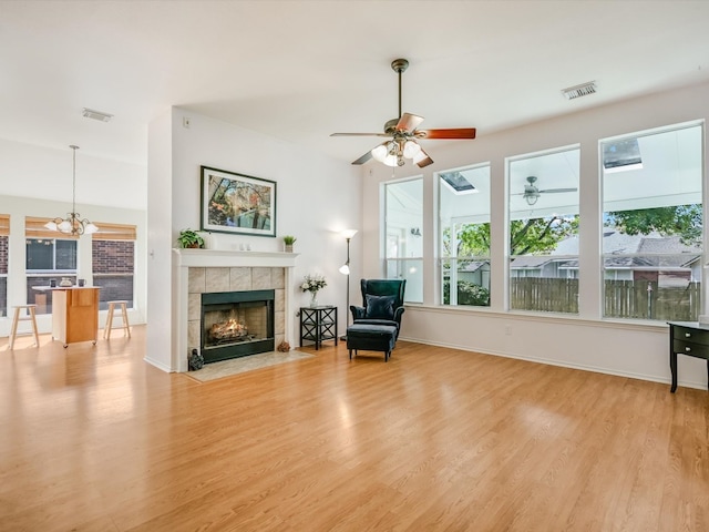 sitting room with a tile fireplace, ceiling fan with notable chandelier, and light hardwood / wood-style flooring