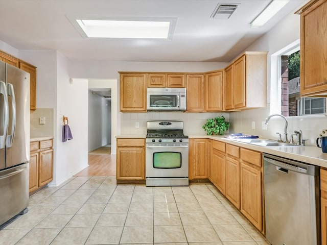 kitchen featuring decorative backsplash, light tile patterned flooring, stainless steel appliances, a skylight, and sink