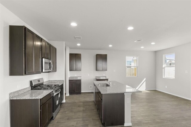 kitchen with light stone countertops, stainless steel appliances, sink, a center island with sink, and dark hardwood / wood-style floors