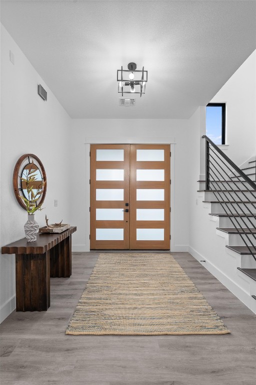 foyer entrance with french doors, hardwood / wood-style flooring, and an inviting chandelier