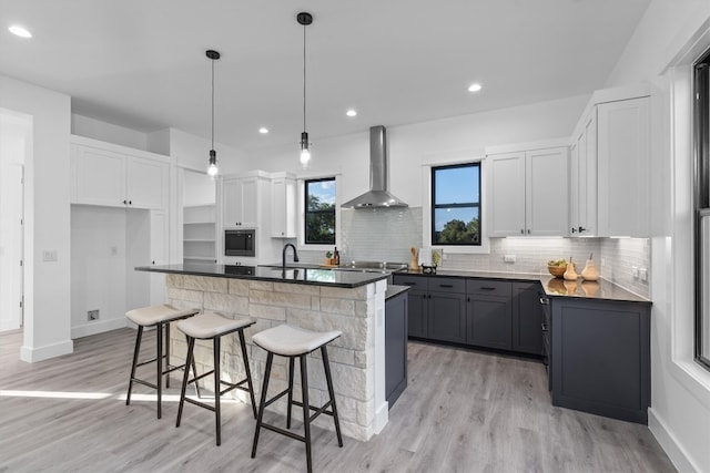 kitchen featuring white cabinetry, a center island, wall chimney exhaust hood, decorative light fixtures, and a kitchen bar