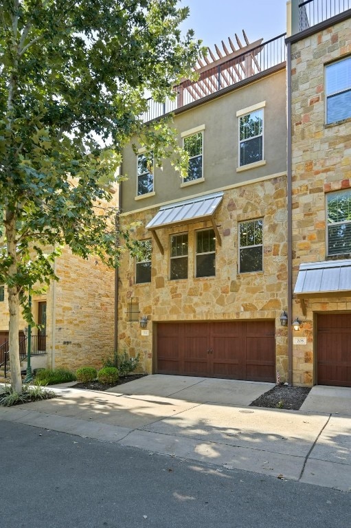 townhome / multi-family property featuring metal roof, an attached garage, stone siding, driveway, and a standing seam roof