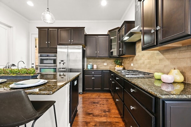 kitchen with decorative light fixtures, dark wood-type flooring, tasteful backsplash, stainless steel appliances, and wall chimney range hood