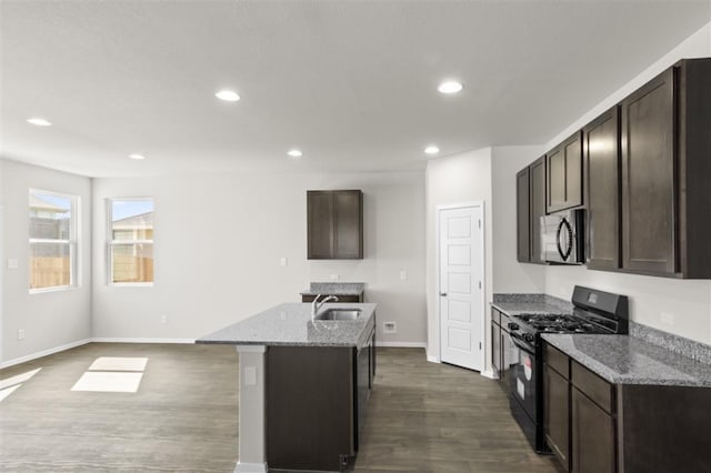 kitchen with a center island with sink, sink, light stone counters, black gas range oven, and dark hardwood / wood-style flooring