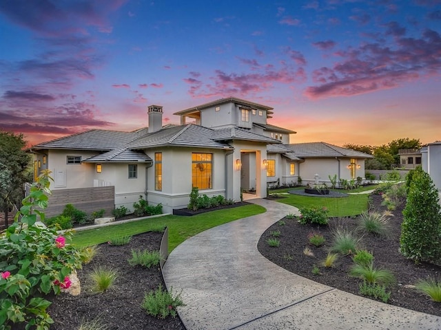 prairie-style home with a tile roof, concrete driveway, a yard, stucco siding, and a chimney