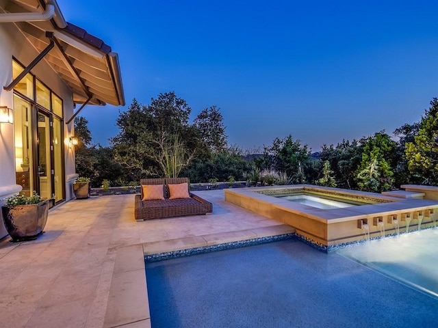 pool at dusk with a patio and an in ground hot tub