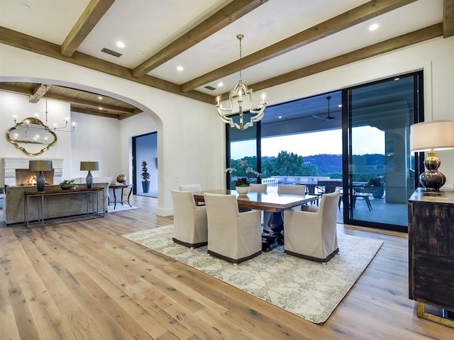 dining space featuring arched walkways, a warm lit fireplace, visible vents, light wood finished floors, and an inviting chandelier