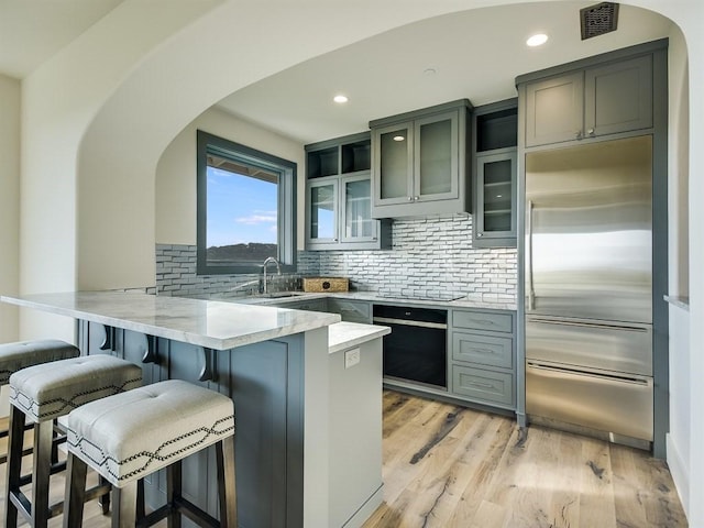 kitchen with a breakfast bar area, a peninsula, built in refrigerator, visible vents, and glass insert cabinets