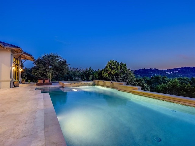 pool at dusk with a patio area and an outdoor pool