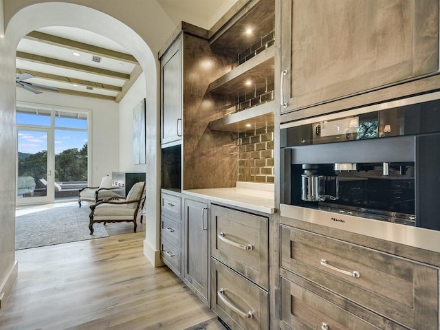 kitchen with arched walkways, decorative backsplash, light wood-style flooring, beamed ceiling, and light countertops