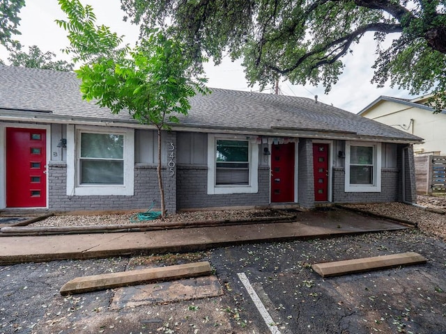 view of front of house featuring uncovered parking, brick siding, and a shingled roof