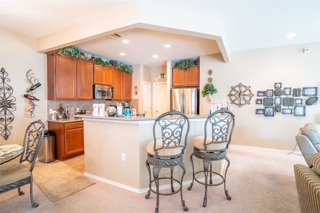 kitchen featuring light carpet, tasteful backsplash, a kitchen breakfast bar, and stainless steel appliances