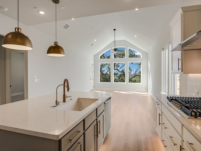 kitchen featuring lofted ceiling, a kitchen island with sink, hanging light fixtures, light hardwood / wood-style flooring, and light stone countertops