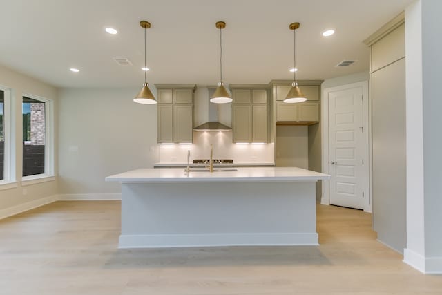 kitchen with an island with sink, light wood-type flooring, and wall chimney range hood