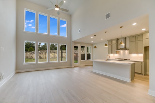 unfurnished living room with light hardwood / wood-style floors, sink, ceiling fan, and a towering ceiling