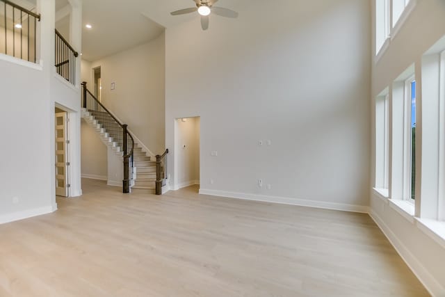 unfurnished living room featuring ceiling fan, light hardwood / wood-style flooring, and a towering ceiling