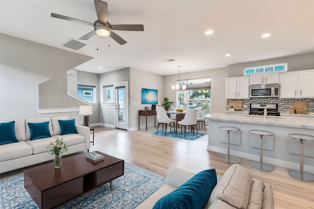 living room with ceiling fan with notable chandelier, sink, and light hardwood / wood-style flooring