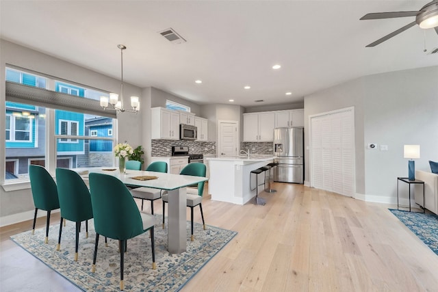 dining area with ceiling fan with notable chandelier, light hardwood / wood-style floors, and sink