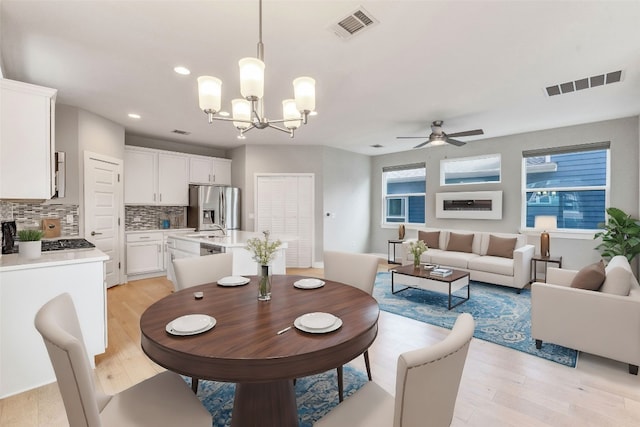 dining room with ceiling fan with notable chandelier, light wood-type flooring, and sink