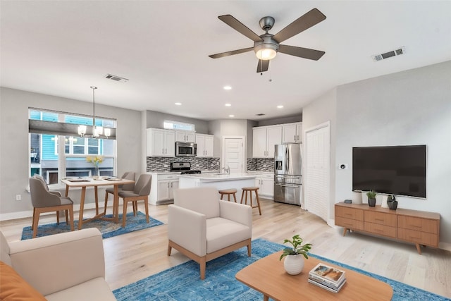 living room with light wood-type flooring, ceiling fan with notable chandelier, and sink