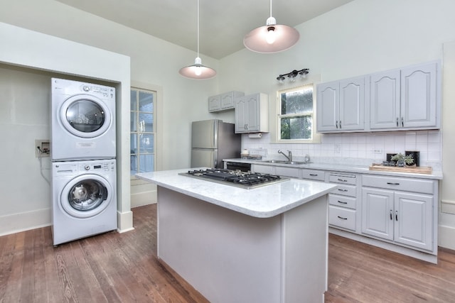 kitchen with stainless steel appliances, stacked washer and dryer, wood finished floors, a sink, and backsplash